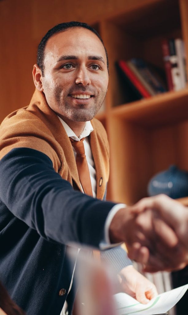 Confident businessman shaking hands in a modern office space, showcasing collaboration and success.